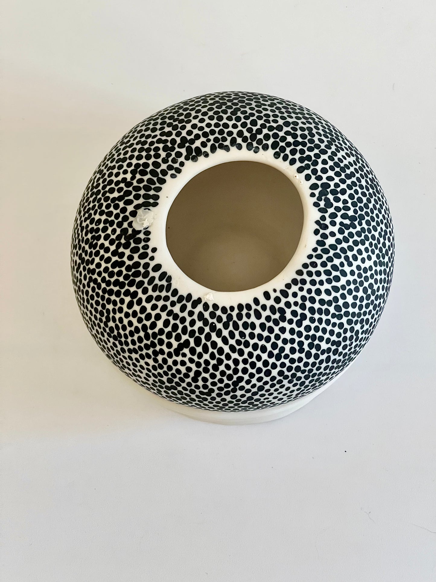 Underside view of Pulse III showing the rounded white porcelain body, dense black dotted decoration , the circular opening at the base. and the artist's stamp