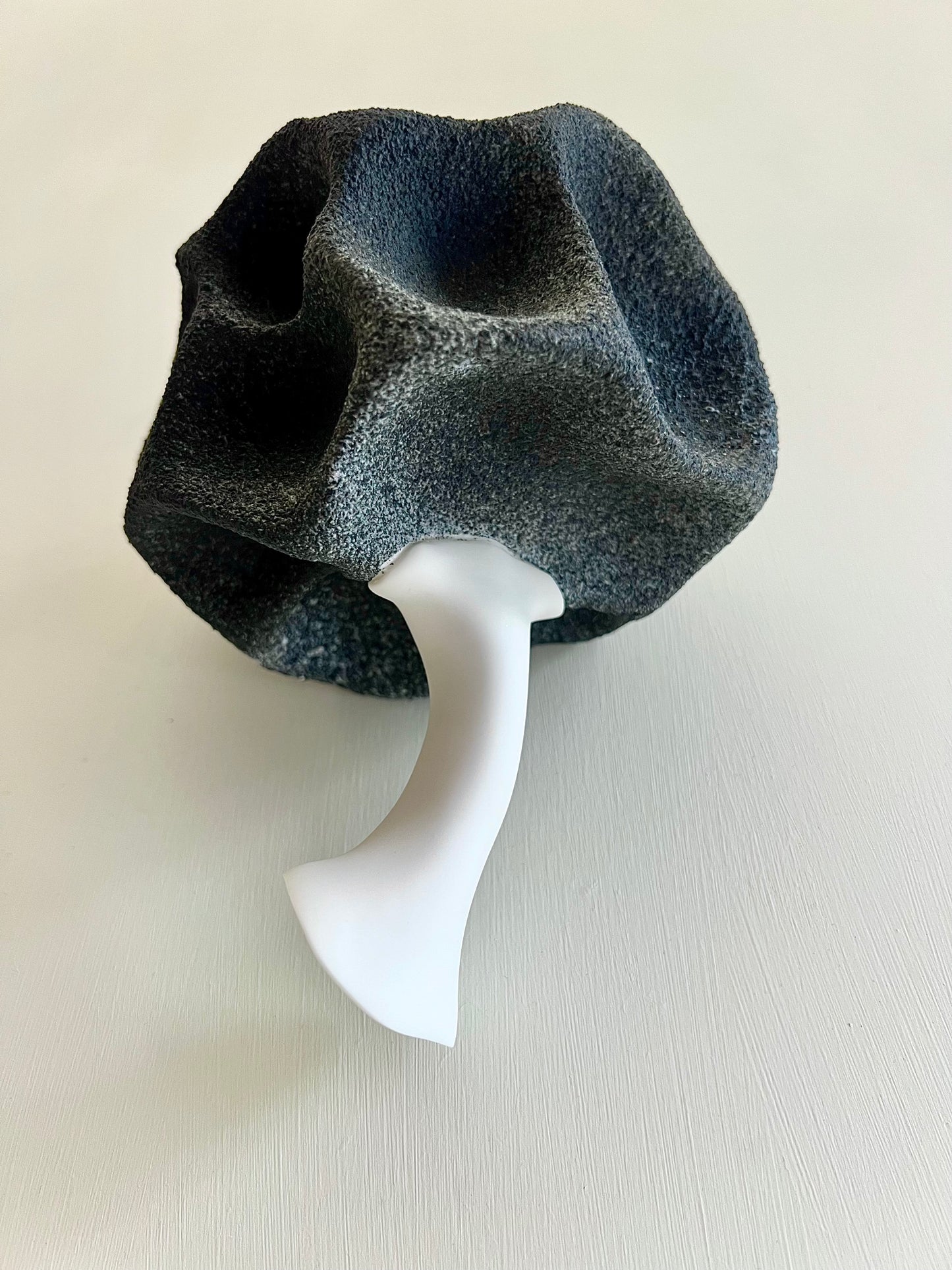 Bottom view of Crazy Wallflower — Black Spore, showing the smooth white porcelain stem and textured dark upper form.
