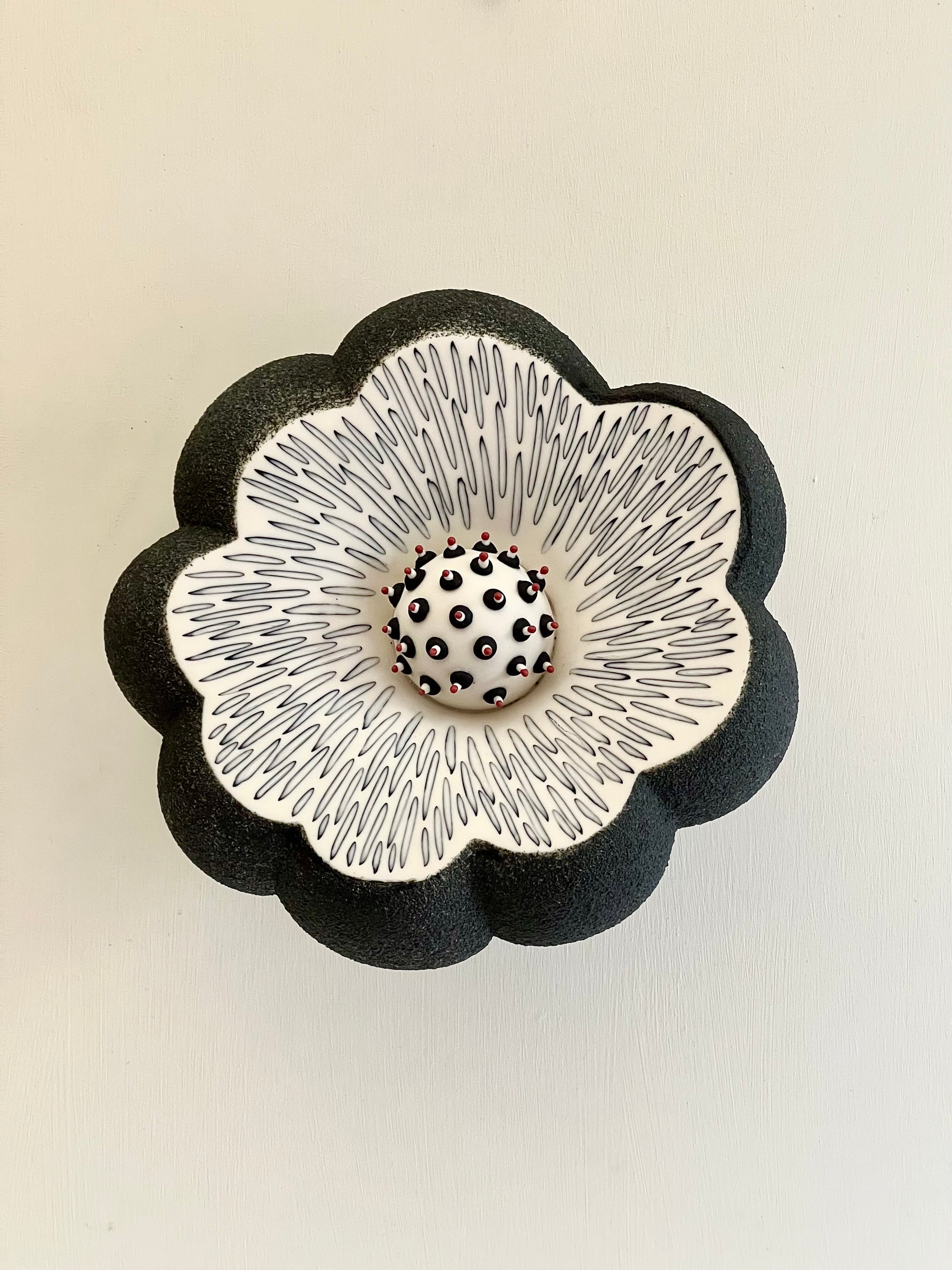 Front view of Crazy Wallflower — Pollen, a handmade porcelain wall sculpture with black textured exterior and white inlaid interior