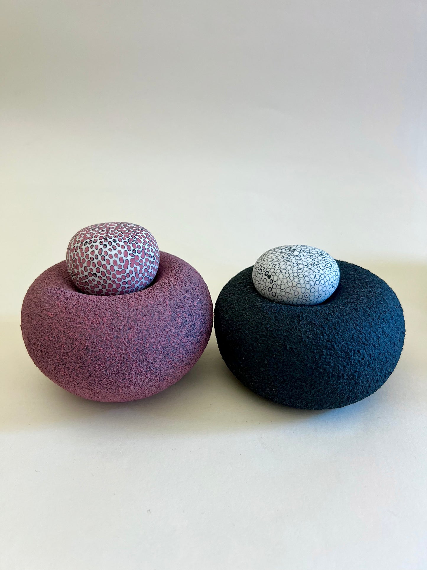 Two handcrafted porcelain elements from the Nest II collection featuring textured black and burgundy bases with hand-inlaid porcelain spheres.