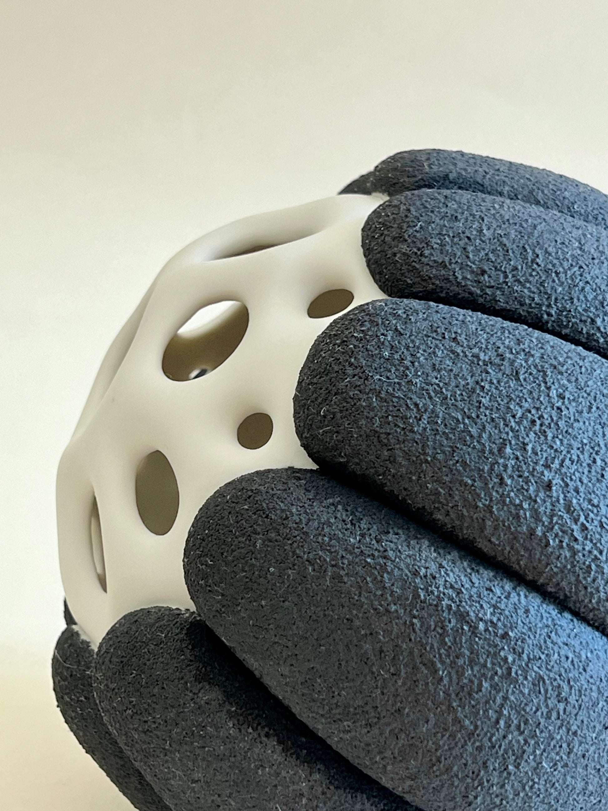 Contemporary porcelain sculpture with pierced white body and rough black porcelain surface.